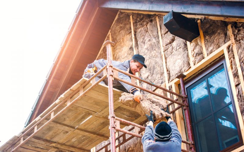 Construction workers standing on scaffold thermally insulating house facade with glass wool.